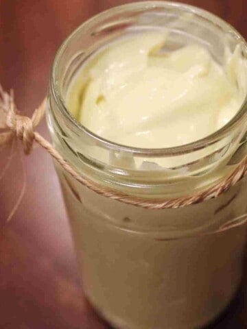 A clear glass jar on a pink background full of smooth, creamy, white mayonnaise.