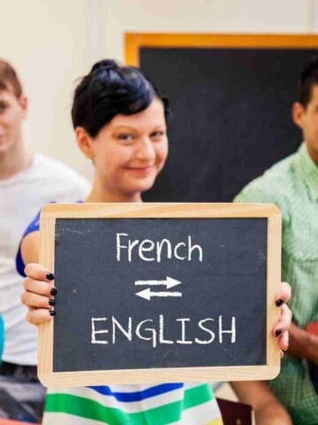 Young woman holding a chalkboard sign with the words French and English written on it with two arrows between them pointing in different directions.