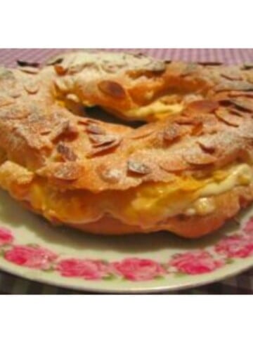 Light brown pastry with almond slices on top and filled with creamy pastry cream on pink floral plate.