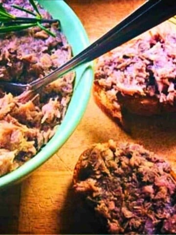 Brown chopped duck meat with spices in a bowl and two baguette slices spread with the mixture.