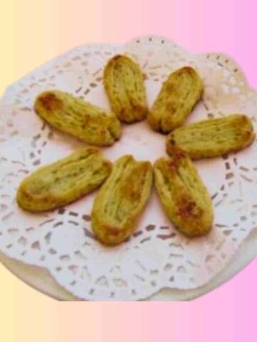 Seven beige puff pastry cookies on a plate laden with a doily.