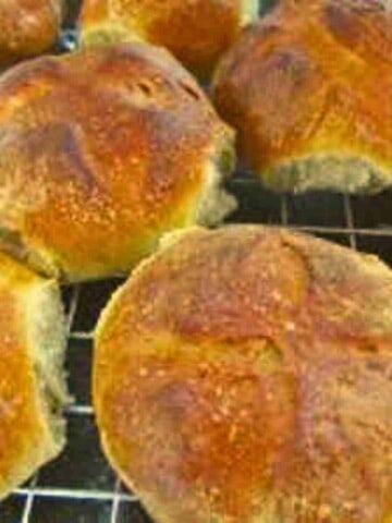 Large brown and beige milk rolls or buns colling on a wire rack.