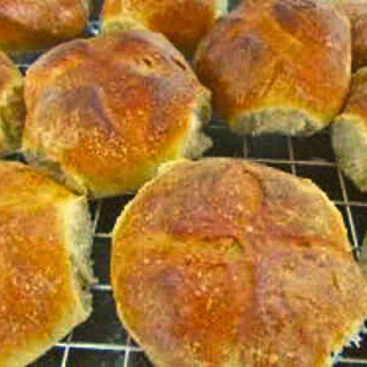 Large brown and beige milk rolls or buns colling on a wire rack.