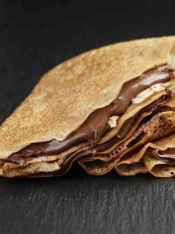 Three crepes folded and filled with chocolate cream on a white plate.