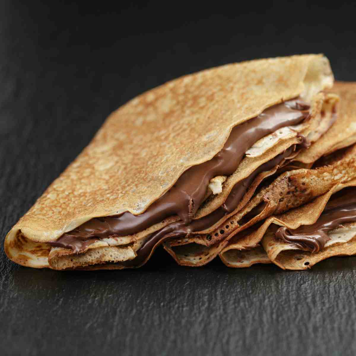 Three crepes folded and filled with chocolate cream on a white plate.