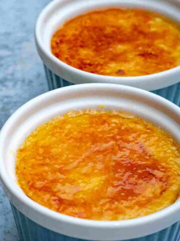 Two small baking dishes, ramekins, filled with custard topped with golden brown and yellow caramel topping.