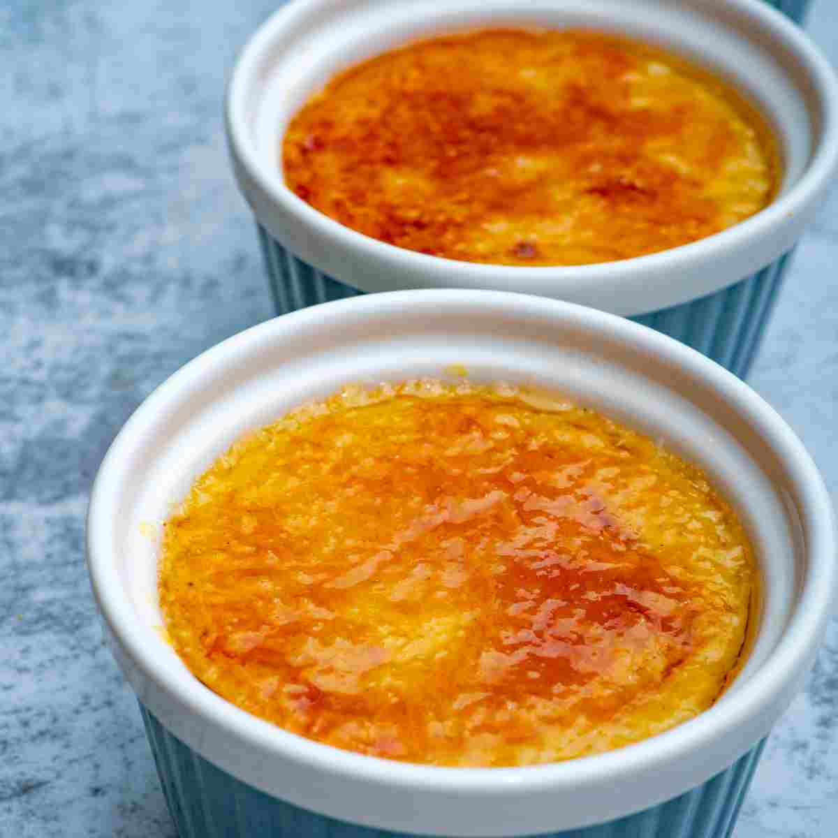 Two small baking dishes, ramekins, filled with custard topped with golden brown and yellow caramel topping.