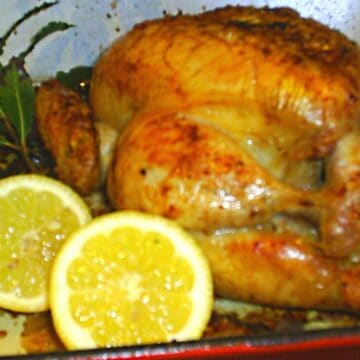 A juicy looking golden roast chicken with lemon and herbs.