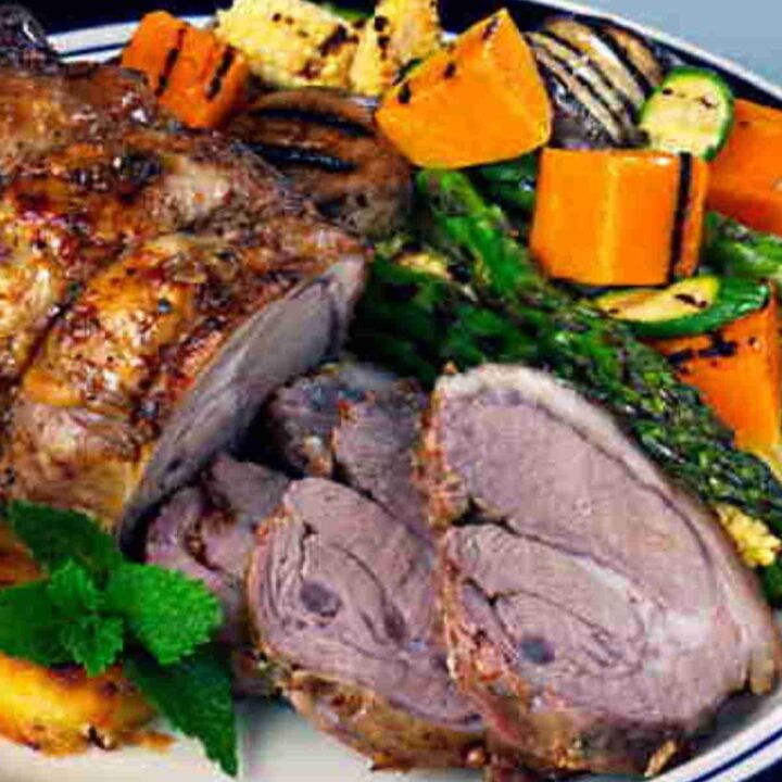 Roasted shoulder of lamb, partly sliced with chunks of sweet potato, baby corn cobs, zucchini, asparagus spears, and mint leaves.
