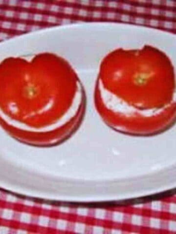 Two red tomatoes sliced in half horizontally and stuffed with white shrimp filling.