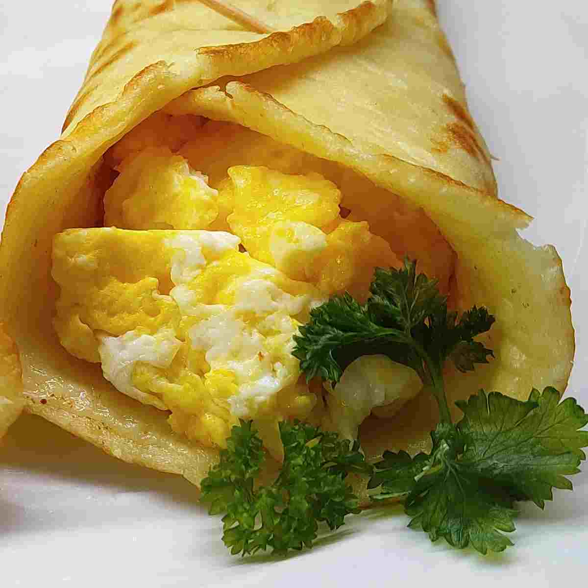 A golden crepe rolled up with yellow and white scrambled egg inside and a sprig of green parsley.