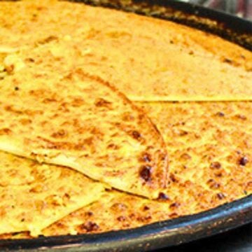 Large black pan filled with golden yellow chickpea flatbread called socca.