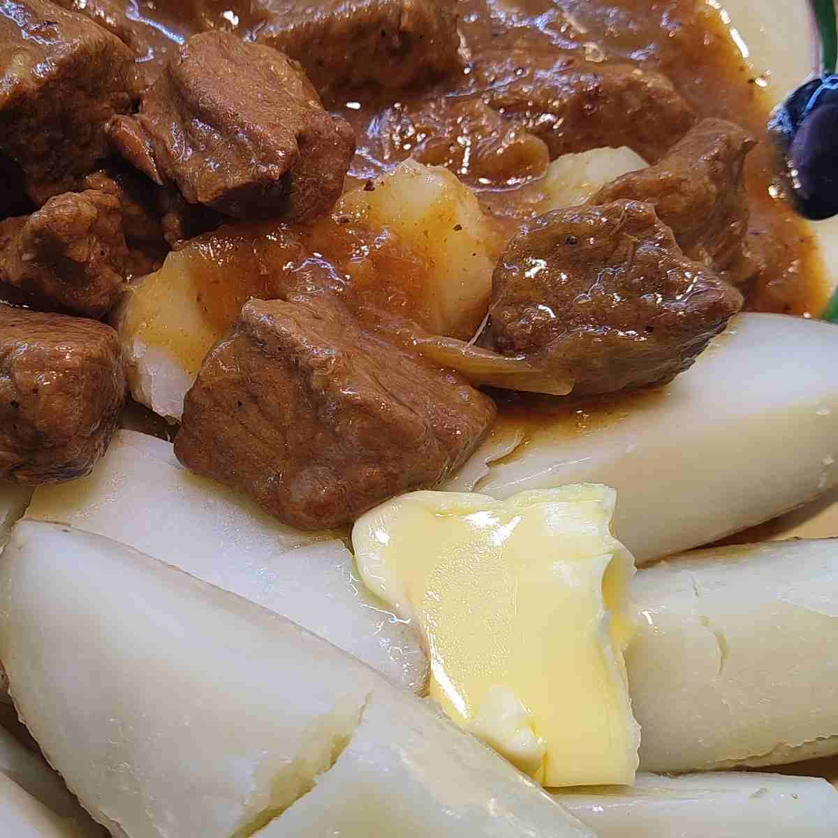 Cooked beef pieces in a brownish gravy and white boiled potato wedges on the side.