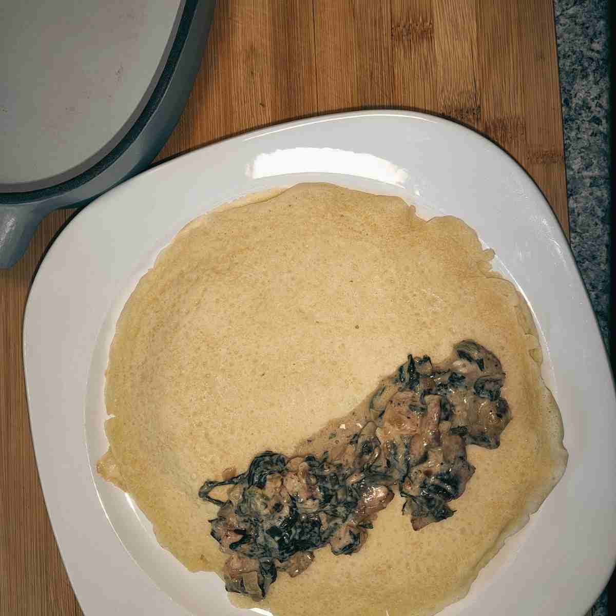 The first crepe with the filling laying on top of it ready to be rolled.