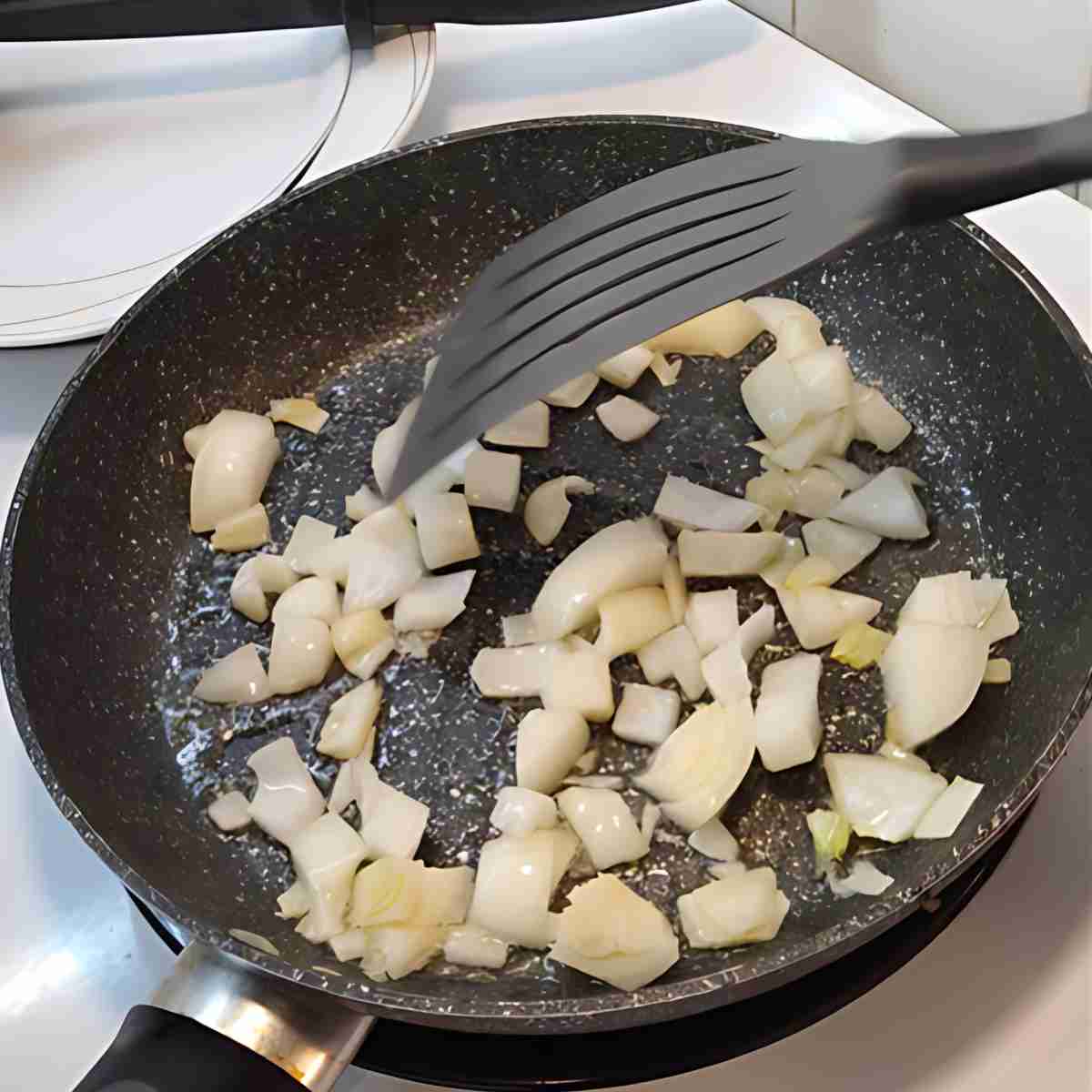 White onions softening in a black non-stick frying pan.