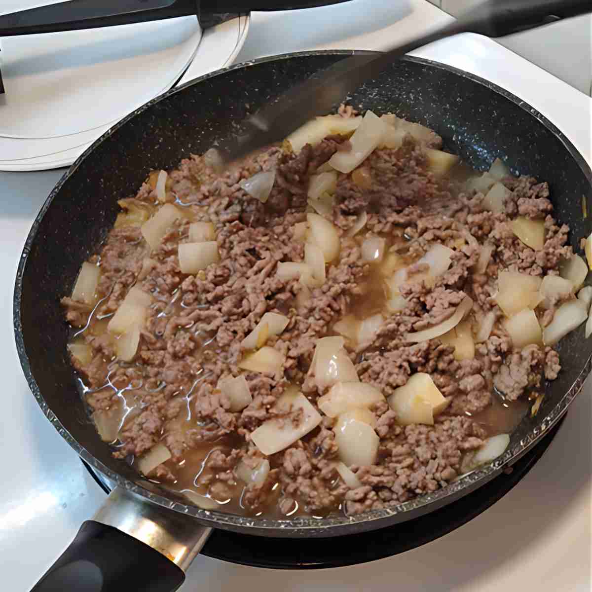 A black pan with brown beef, white onion in a sauce.