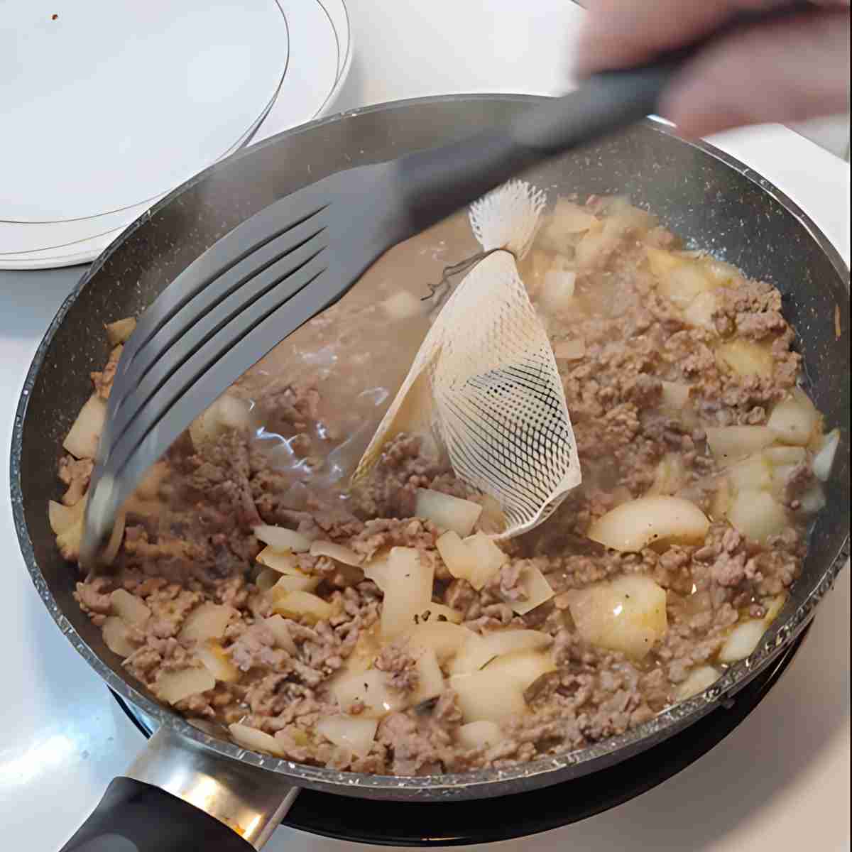 Brown ground beef in a frying pan with white onions, and a nylon bag with spices.