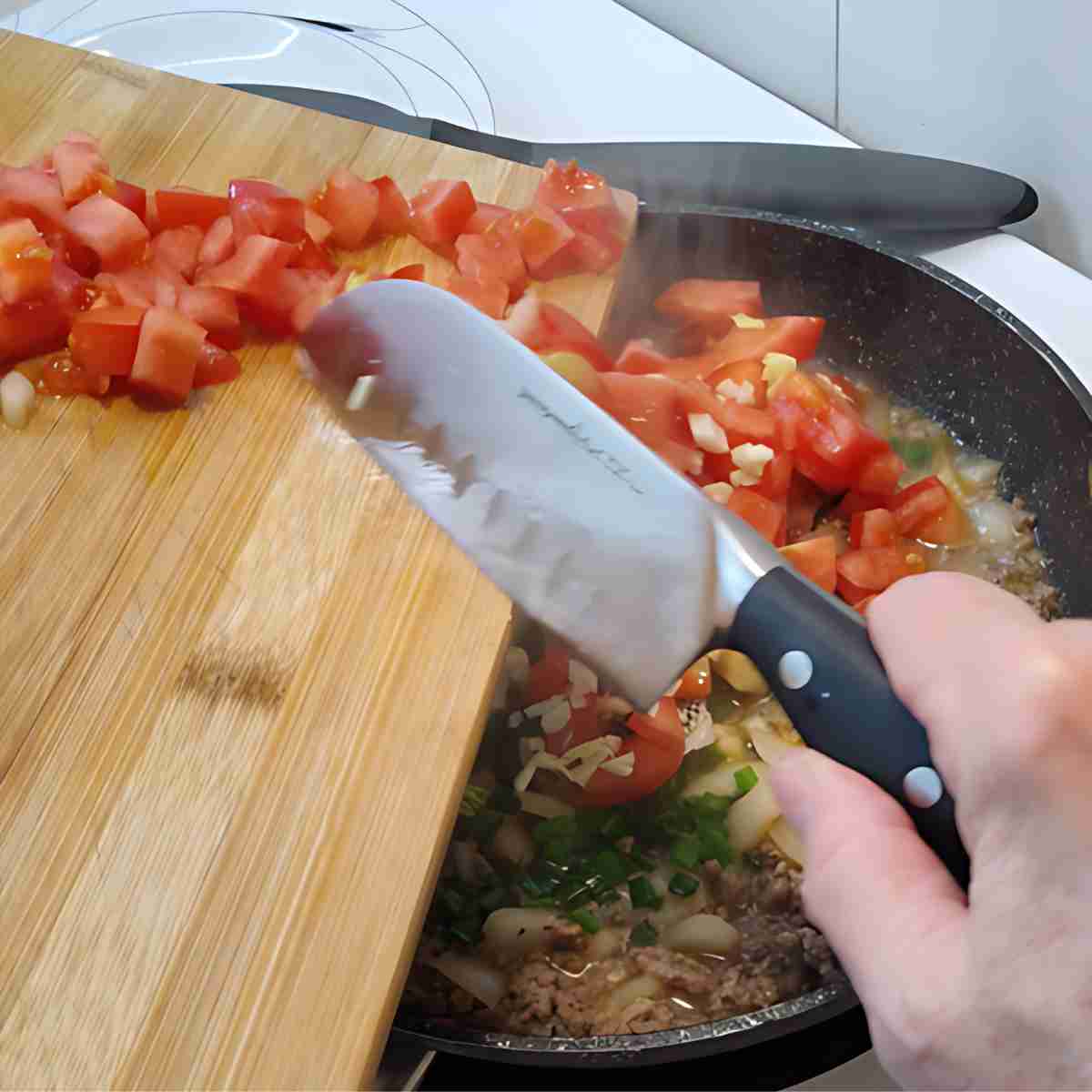 Red and white vegetables being added to a black pan with brown meat cooking.