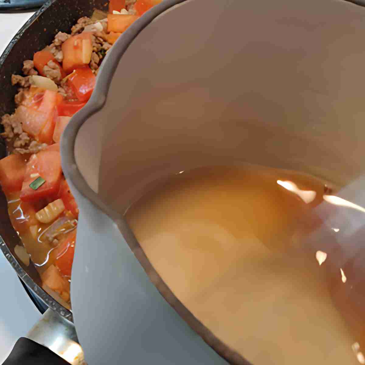 A brown sauce in a white and blue cast iron pan with a colorful food pan behind it.