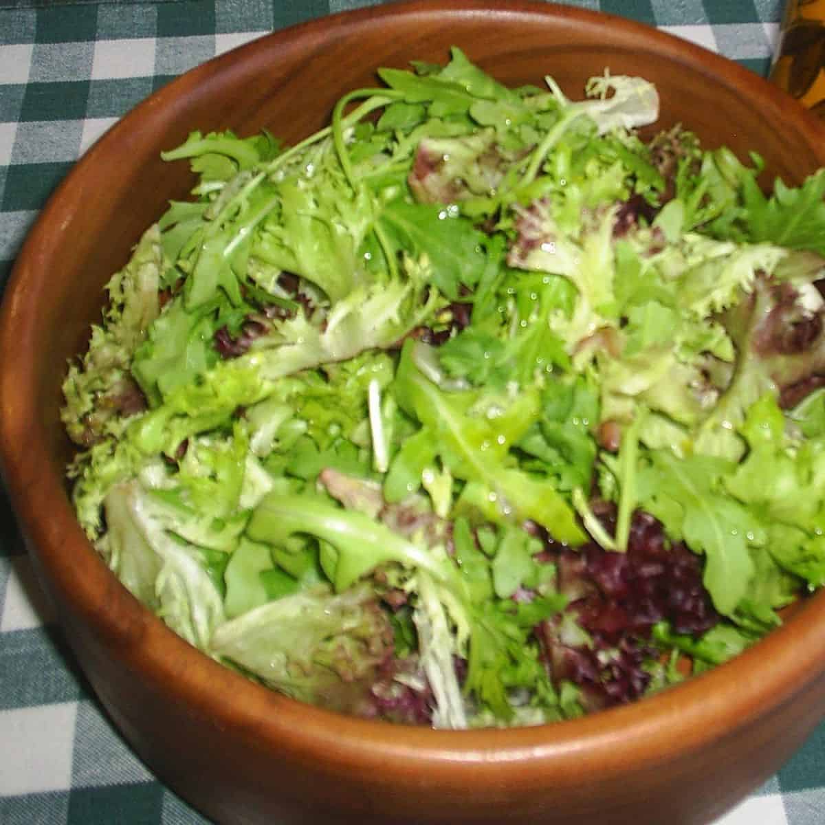 A brown wooden bowl with a variety of salad greens.