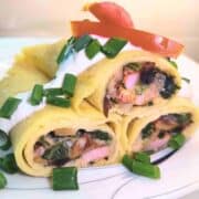 Three stuffed crepes piled on top of one another, garnished with red tomato and green chives on white sour cream.