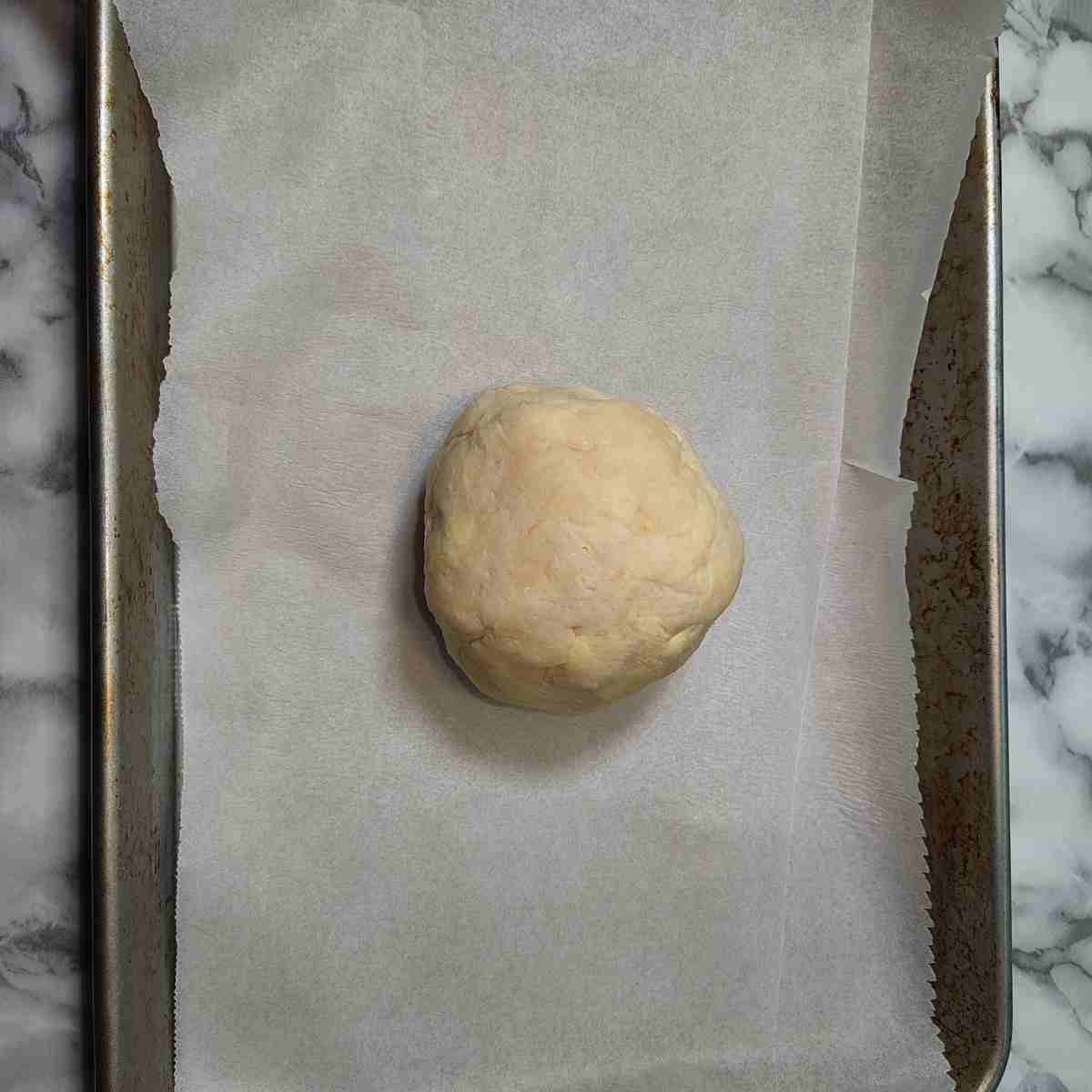 Beige pastry ball on a white parchment lined silver cookie sheet.
