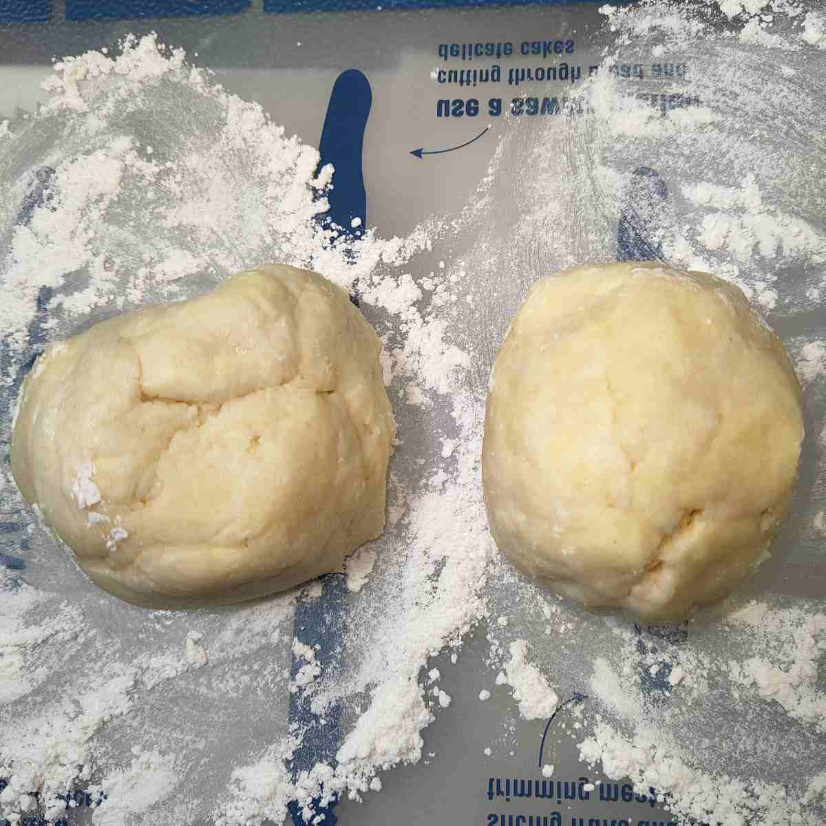 Two beige balls of pastry dough on a floured silicone mat.