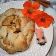 A light brown galette on a white plate with orange flowers on the side and a pink French bull dog figurine.