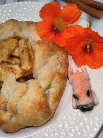 A light brown galette on a white plate with orange flowers on the side and a pink French bull dog figurine.