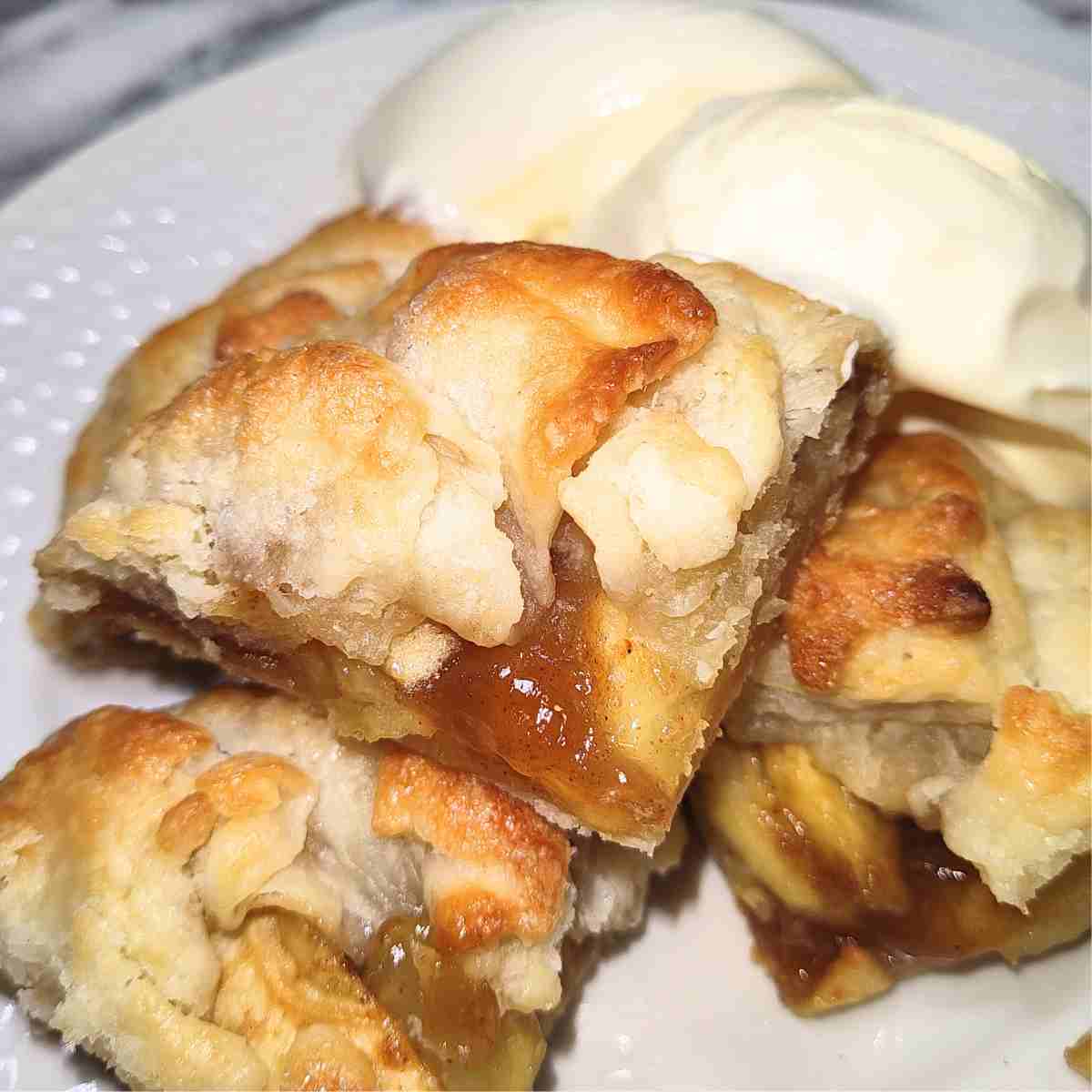 One beige and golden brown galette cut in fours on a white plate with white ice cream on the side.