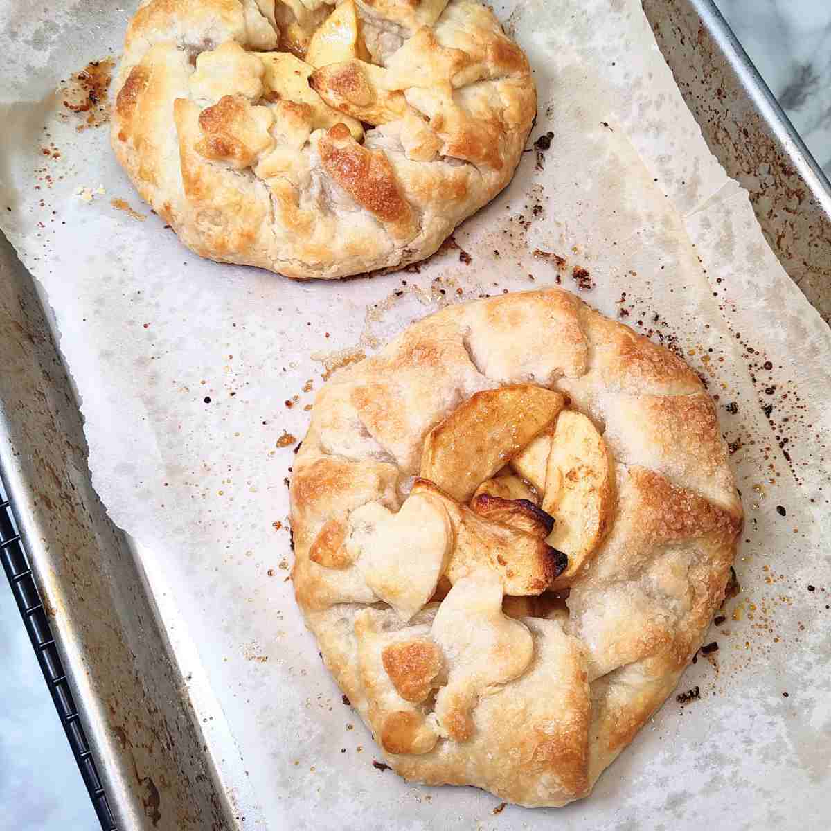 Two brown, beige, and yellow galettes cooling on the cookie sheet.