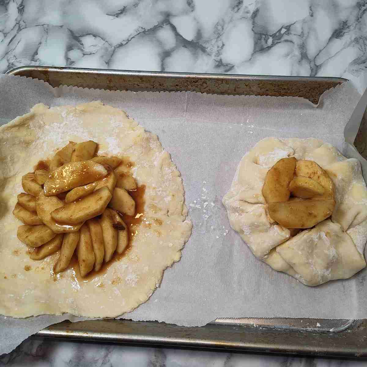 Two beige galette pastry shells, one filled and folded and the other one rolled flat still filled with brown runny apple filling.