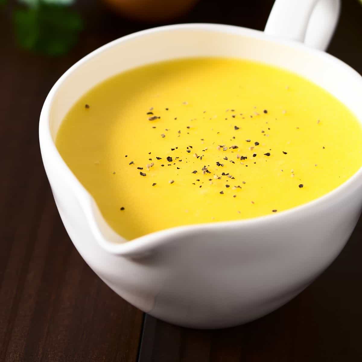 White creamer filled with a bright yellow sauce, sprinkled with black bits.