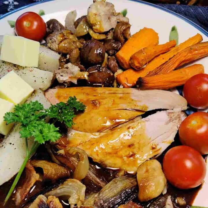 Colorful roast turkey dinner on a plate drizzled with dark brown gravy.