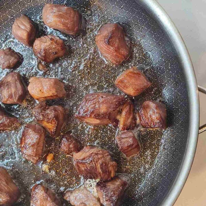 Silver sautee pan with browning beef chunks.