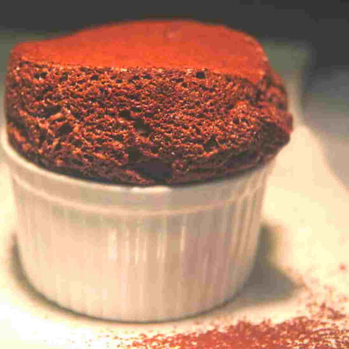 Dark chocolate dessert full of air bubbles in a white bowl on a white plate with brown cocoa sprinkled on it.
