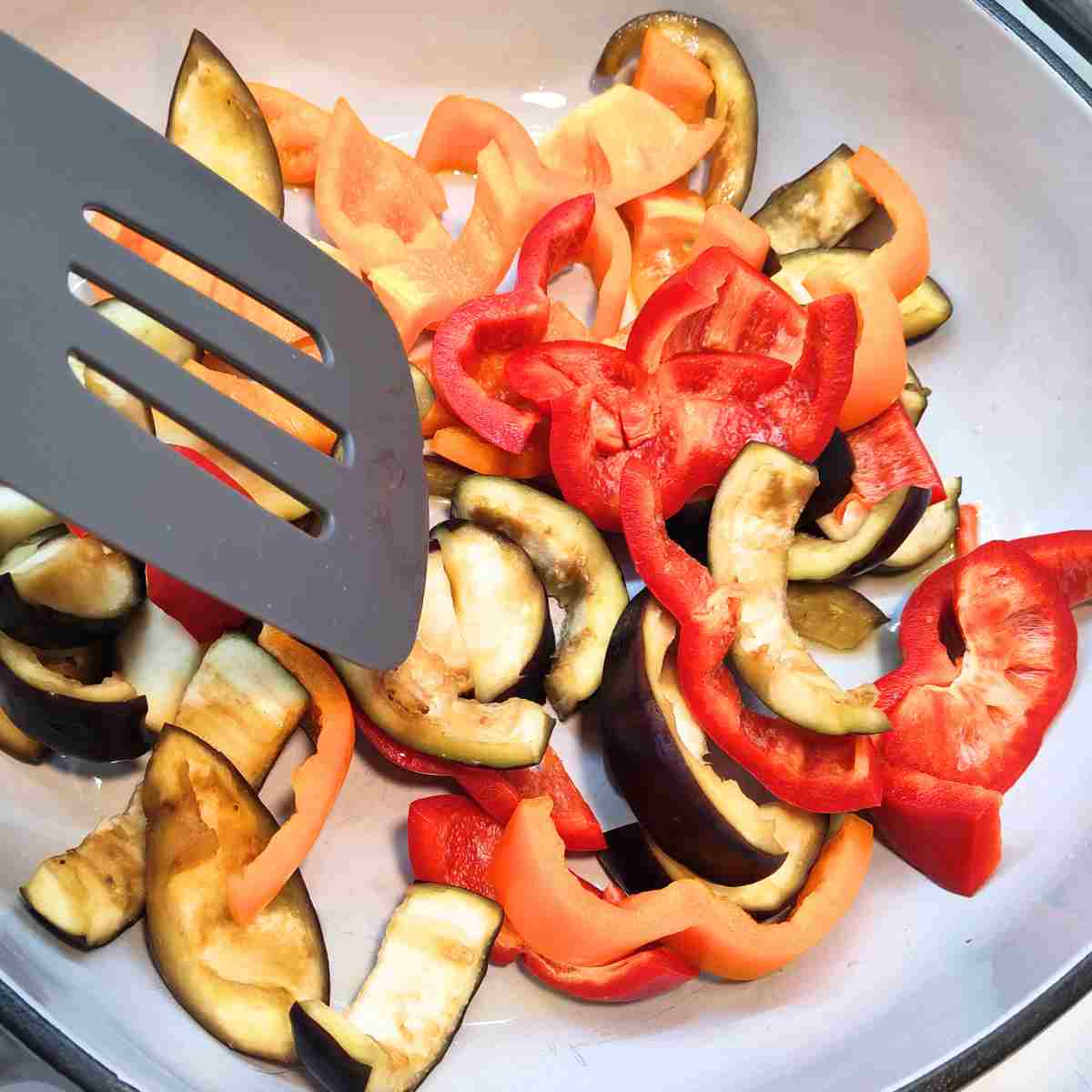 Black and yellow eggplant with yellow and red peppers simmering in a pot.