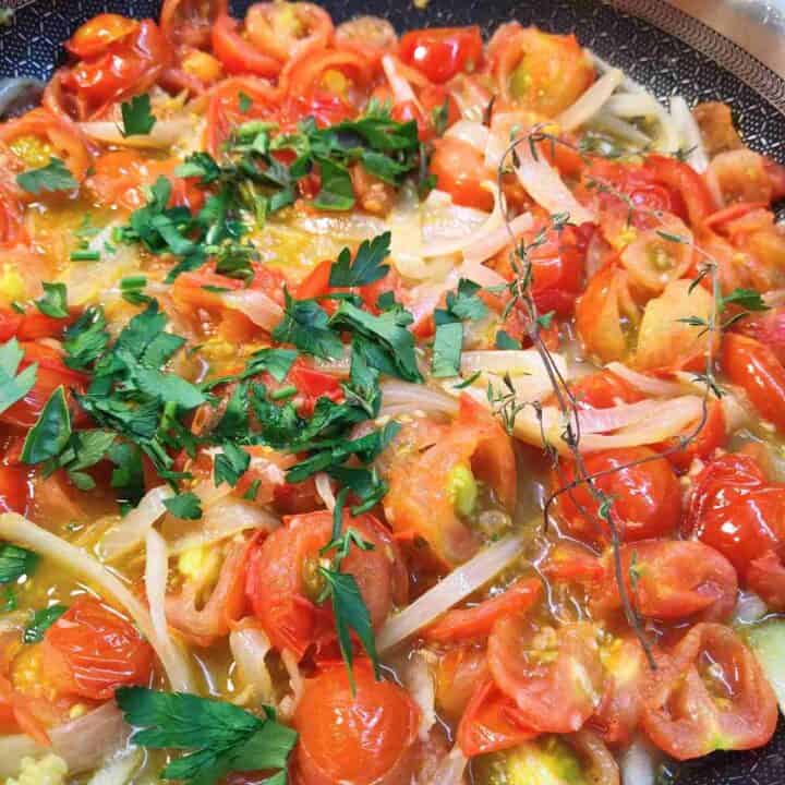 Orange and red vegetables in pan with green parsley, basil, and thyme on top.