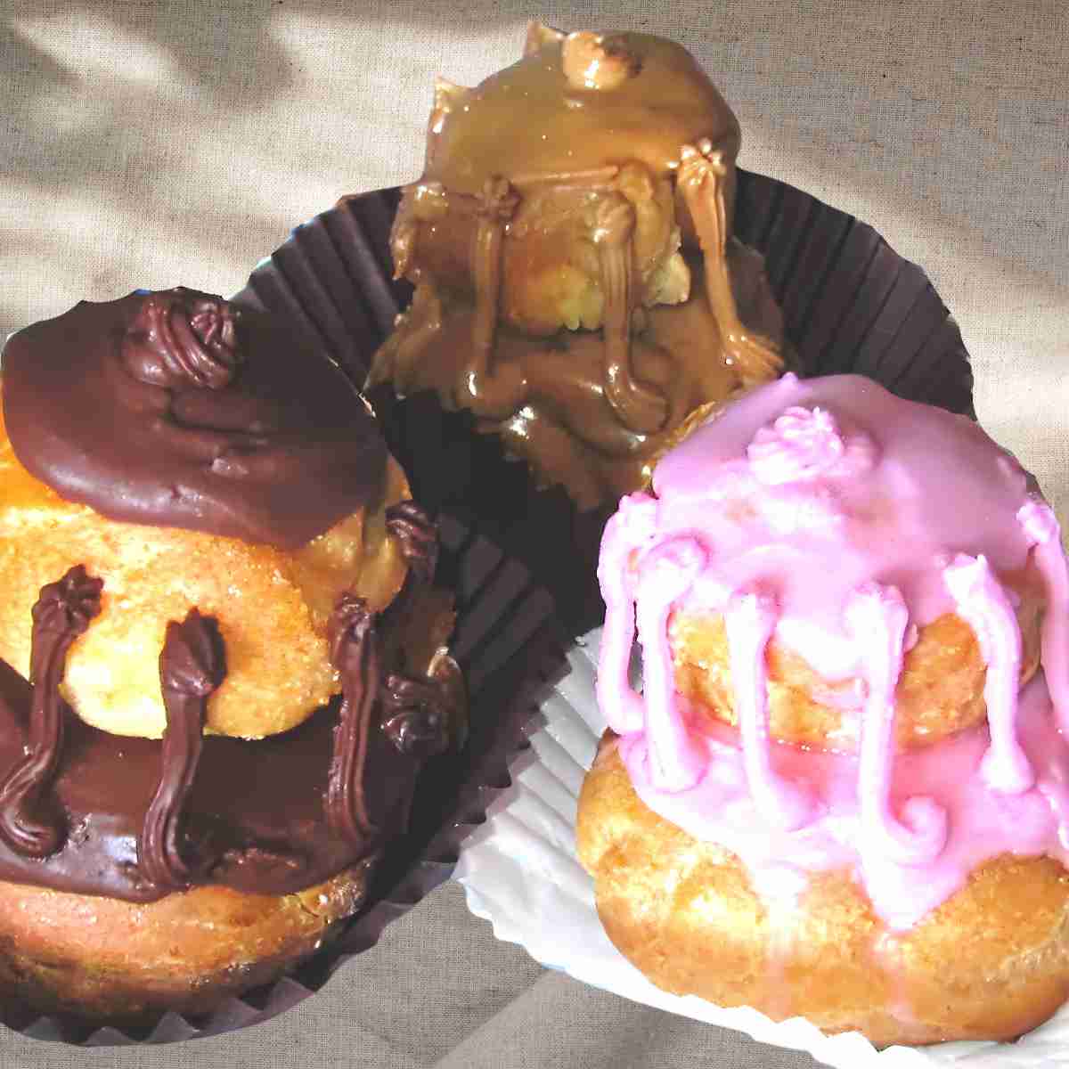 Three cream puffs covered in buttercream icing in various flavors cherry, butterscotch, and chocolate.