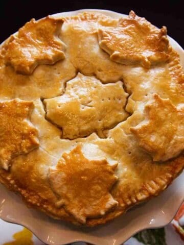 A golden yellow and brown meat pie with maple leaf pastry cutouts as decorations.