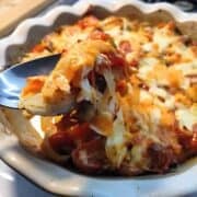 A baking dish filled with orange and white melted cheese on red and white vegetables.