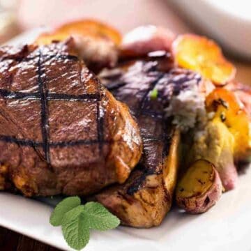 Cooked dark lamb chops with yellow roasted potatos and green mint leaves.