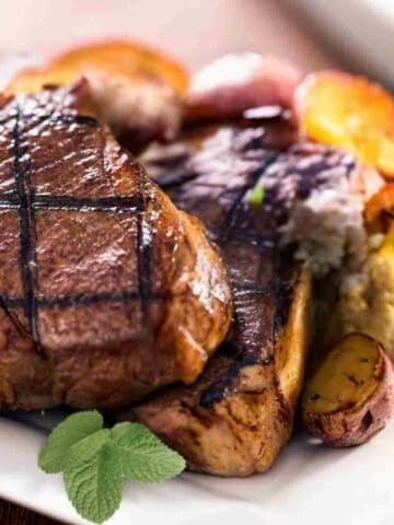 Cooked dark lamb chops with yellow roasted potatos and green mint leaves.