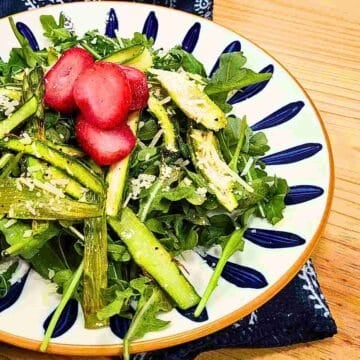 A vegetable salad plated with lemon salad dressing, topped with parmesan cheese, and garnished with strawberries.