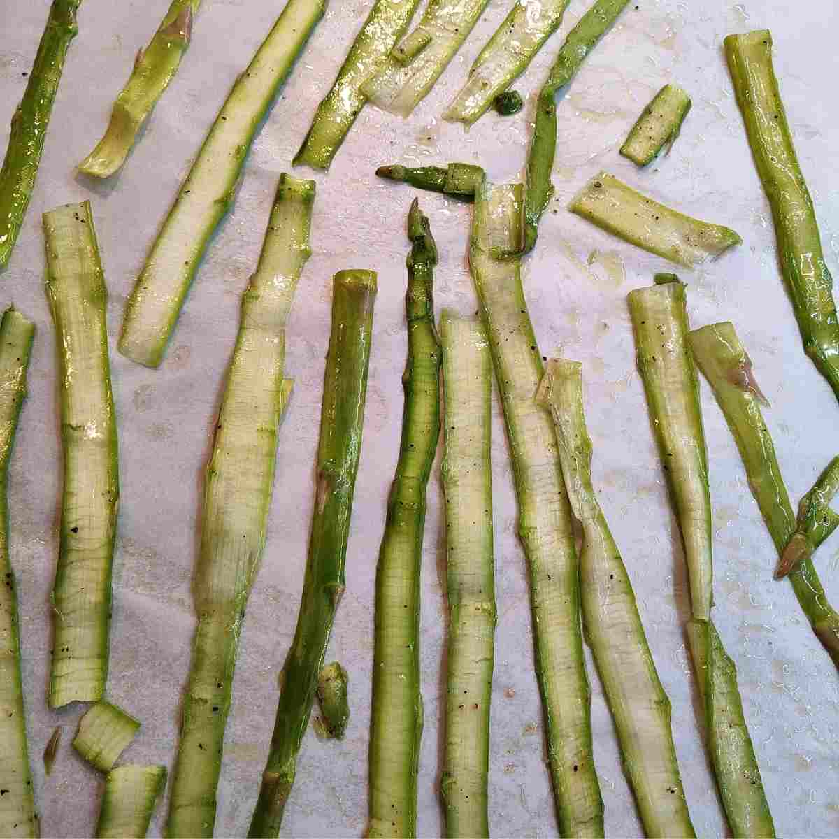 Ribbons of asparagus laying on a parchment paper lined baking sheet ready for roasting.