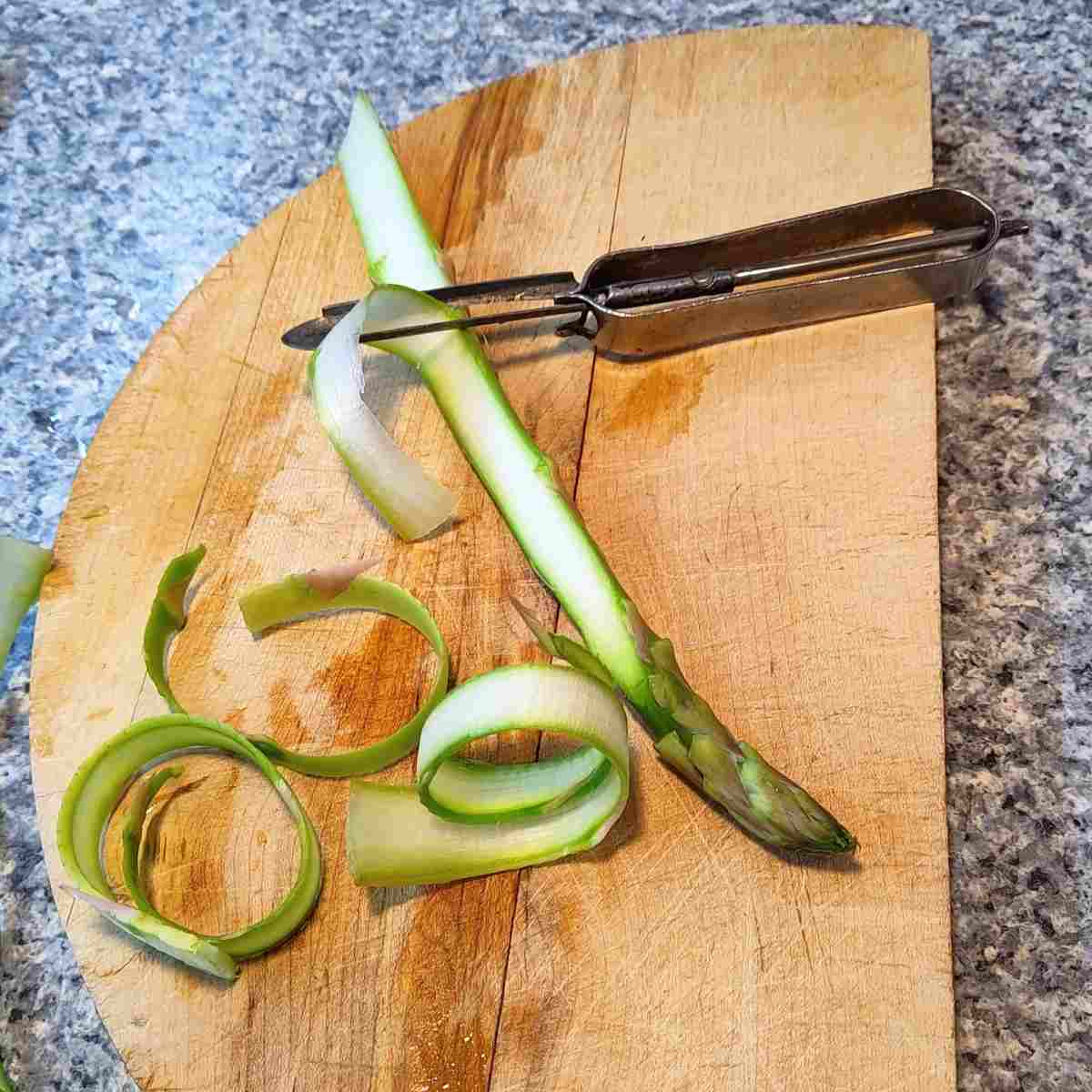 Shaving asparagus spear with a vegetable peeler.