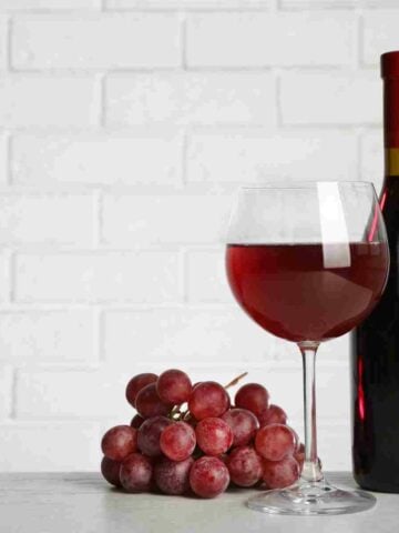 A fine glass of burgundy pinot noir with a full bottle and grapes.