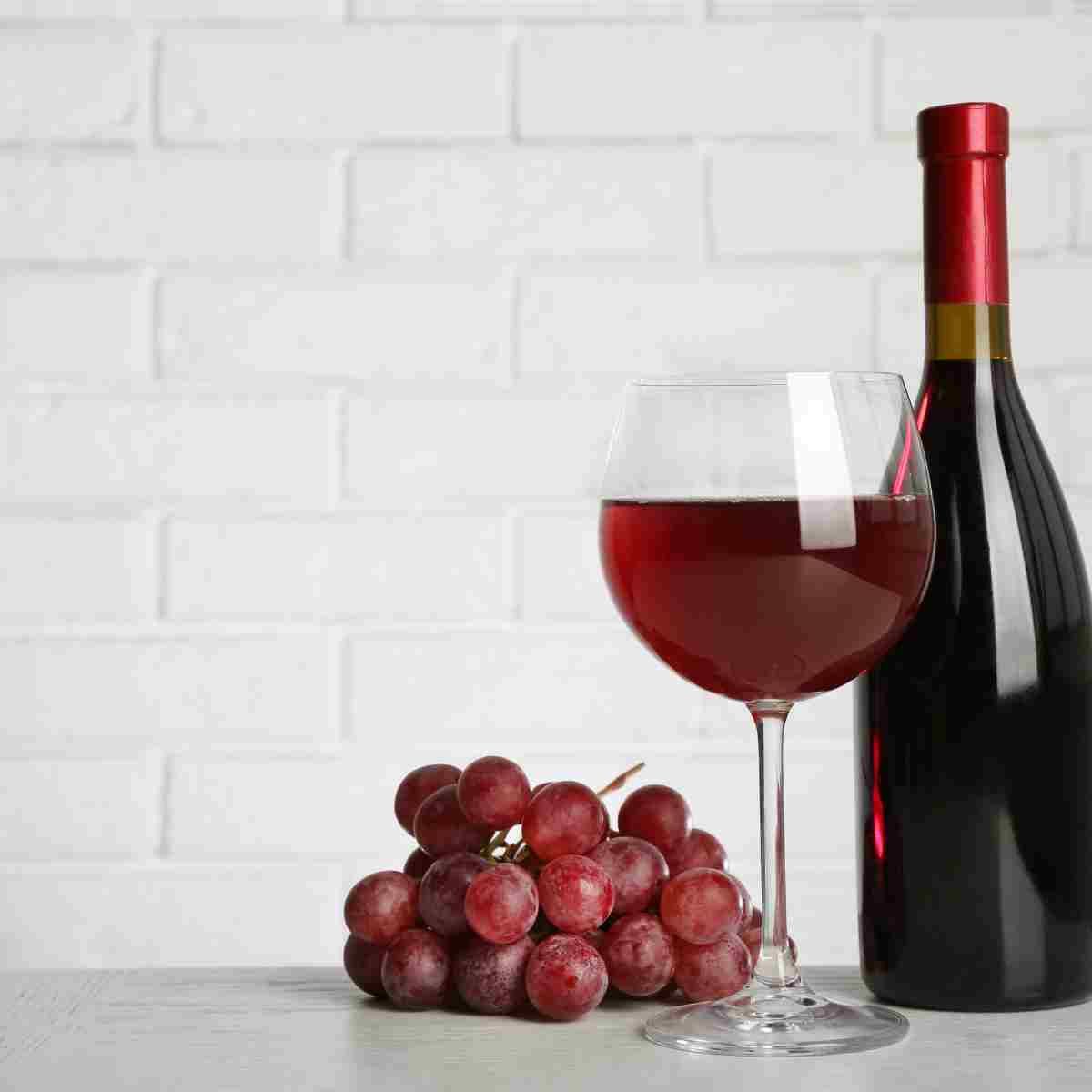 A fine glass of burgundy pinot noir with a full bottle and grapes.