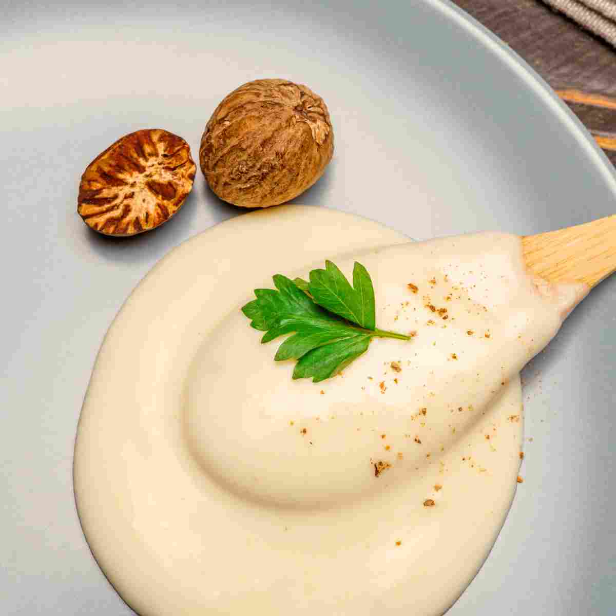 A silky, smooth spoonful of béchamel sauce on a plate with nutmeg seeds.